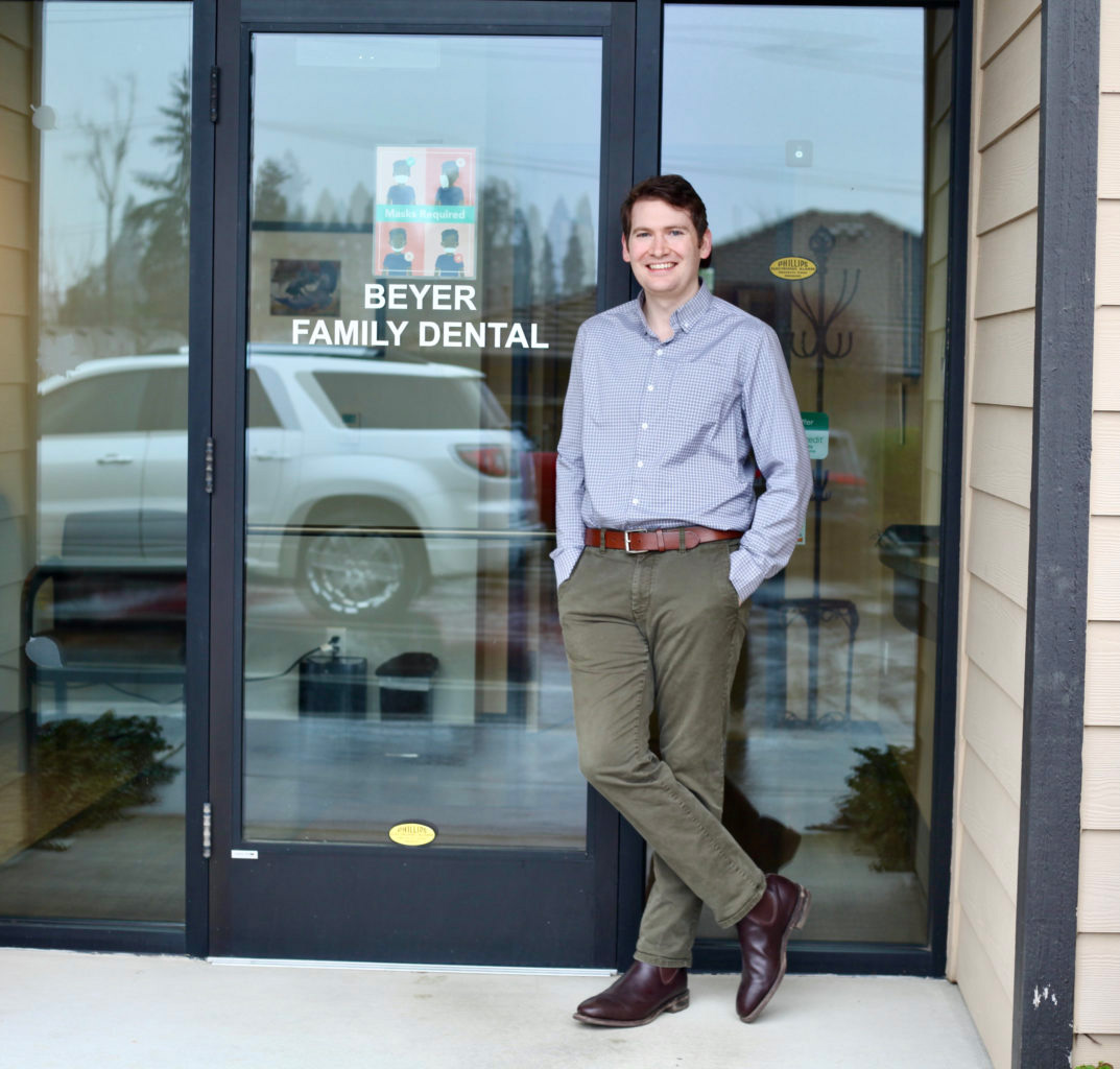 A man stands in front of a dental clinic entrance, smiling and posing for the camera.