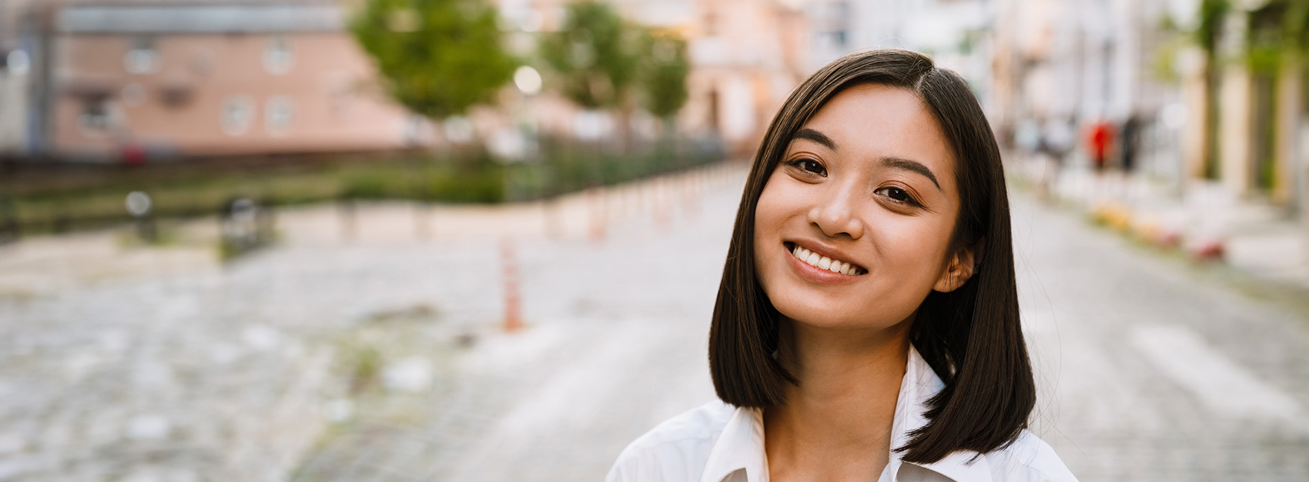 The image is a photograph of a woman with light skin, smiling at the camera. She appears to be in her late twenties or early thirties and has long hair. Her eyes are looking directly at the camera, and she is holding up her index finger near her mouth as if she s making a point or emphasizing something. The background is plain and light-colored, which suggests that this could be a stock photo used for various purposes such as advertising, personal branding, or lifestyle content.