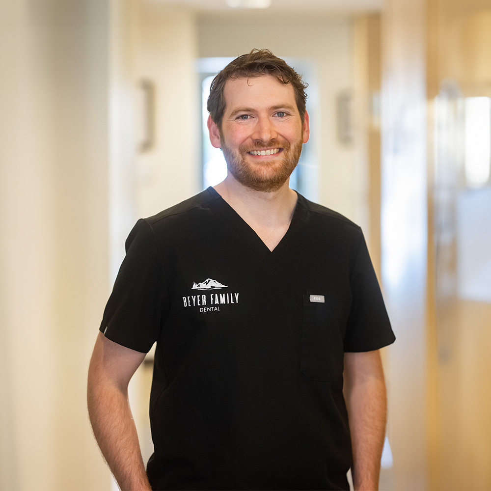 The image shows a man standing in an indoor setting, wearing a black shirt with the word  DOCTOR  visible on it and a name tag that reads  JASON,  suggesting he is a medical professional.