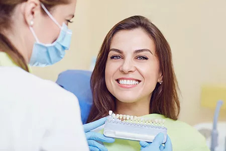 A dental hygienist is assisting a smiling woman with her oral care, using a dental device.