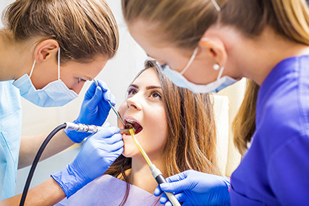 Dental hygienist performing a dental cleaning with a patient in the chair, surrounded by dental equipment and tools.