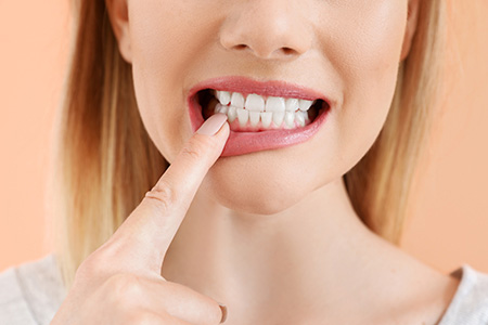 A woman with a toothbrush in her mouth, holding it up to her teeth.