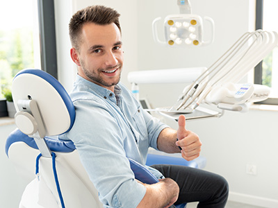 Man in a dental office, smiling and giving thumbs up.